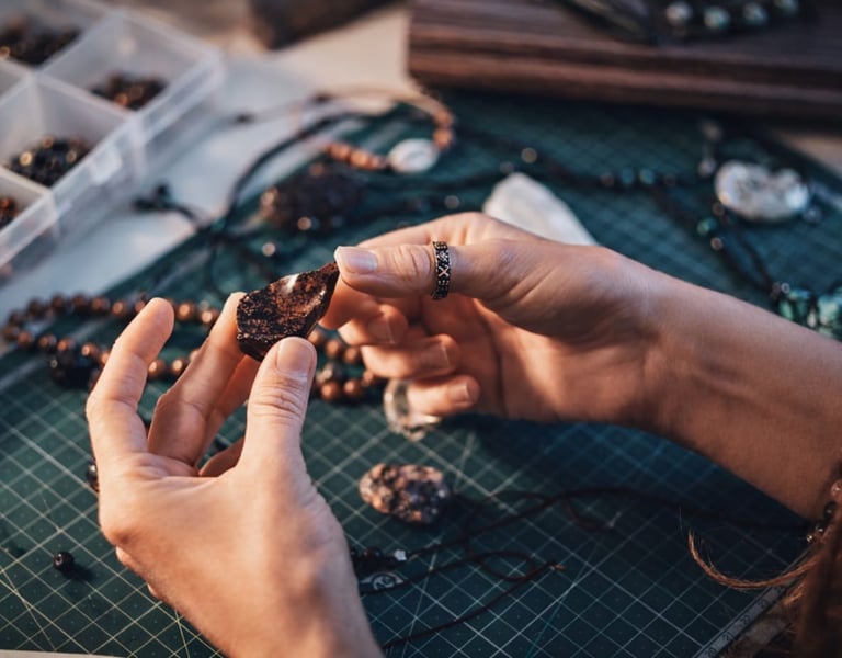 Manos de artesana sosteniendo piedra natural oscura sobre mesa de corte verde con herramientas y cue