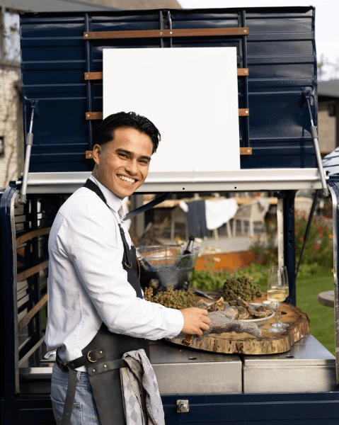 Vrolijk lachende medewerker opent oesters voor de Xagis tuc-tuc foodtruck.