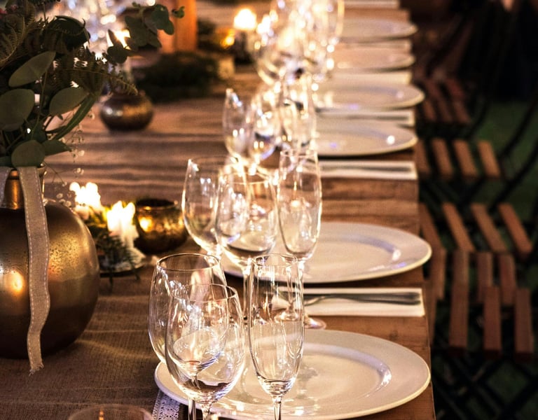 Elegant long wooden banquet table set with white plates, wine glasses, and candles for a wedding reception.