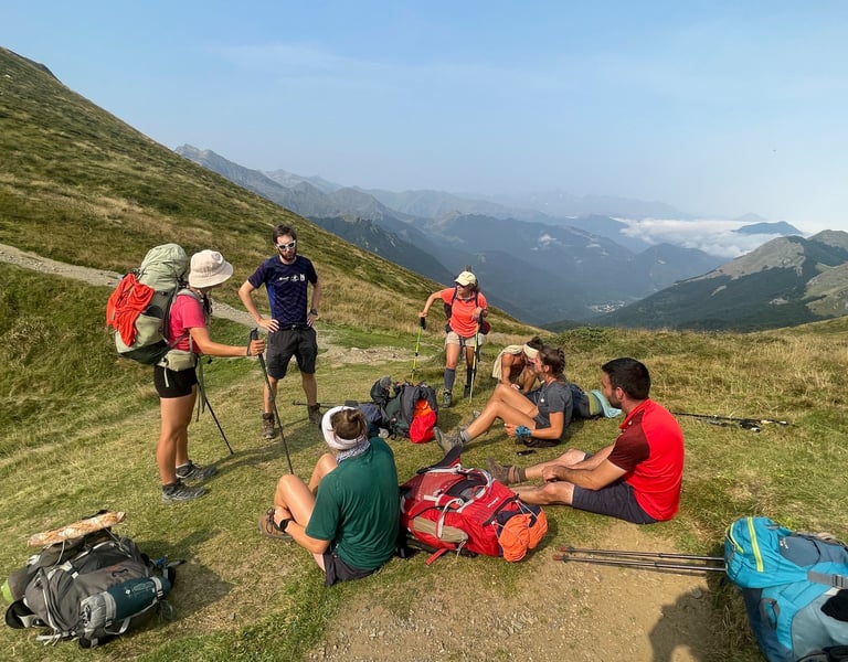 Un groupe de randonneurs, sacs à dos et bâtons de marche à la main, se repose sur une crête