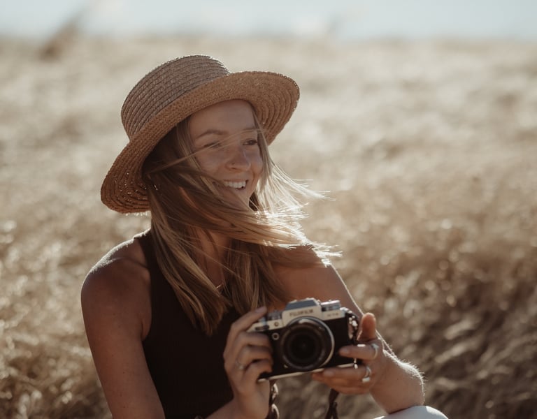 Portrait of a woman in a hat, she is holding a camera and smiling