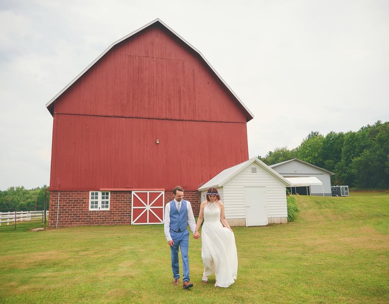 a bride and groom standing walking away from a barn
