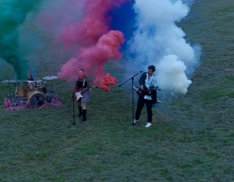Groupe de musique de trois personnes dans un champ avec fumigènes colorés filmé par drone