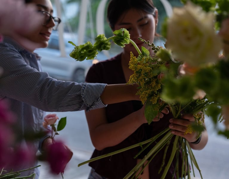 Two professional florists arranging a fresh bouquet of green and yellow flowers in a flower shop.