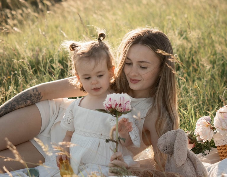 A mother and young daughter in white dresses enjoy a summer picnic in a sunny meadow.