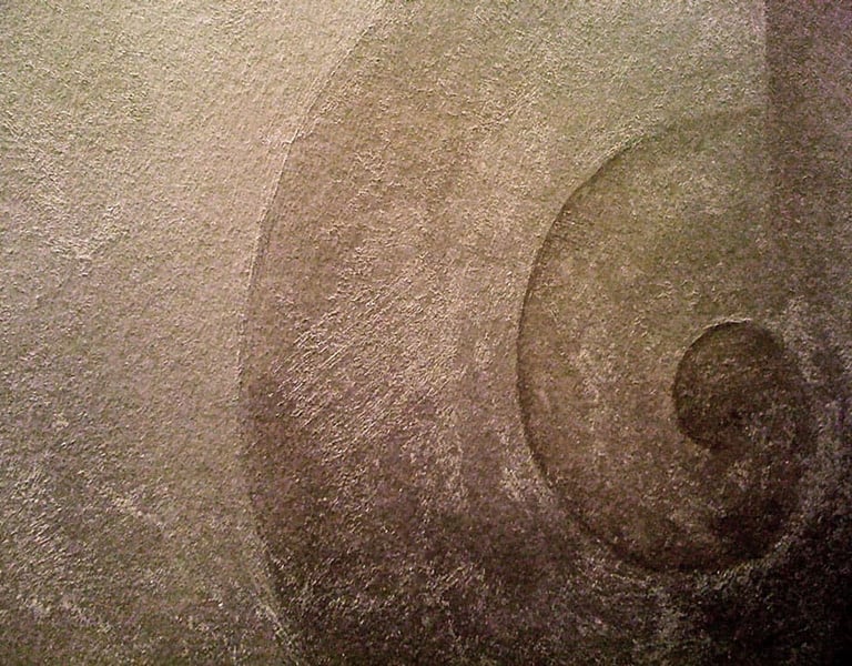 Close-up of a snail swirl painted with warm silver paint in a gritty texture.
