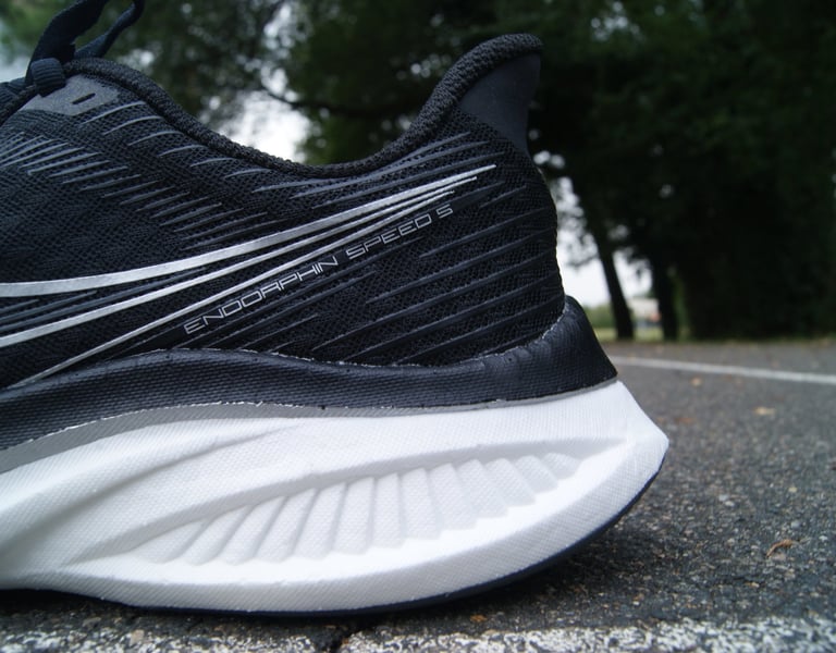 Close-up of a black Saucony Endorphin Speed 3 running shoe with white foam midsole on a paved road.