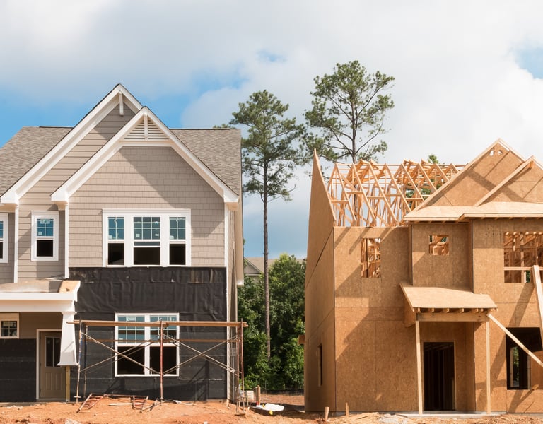 Two homes side by side showing different construction phases, from framing to near-complete exterior