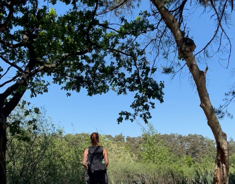Anneke met rugzak, uitkijkend over een vijver, omringd door bomen