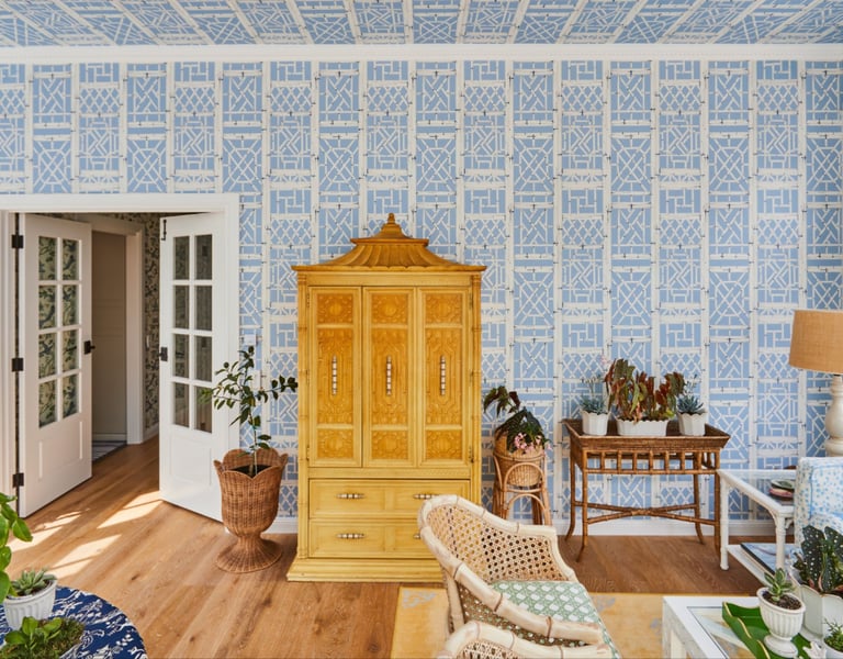 Elegant sunroom featuring blue geometric lattice wallpaper, an ornate yellow Chinoiserie armoire, and lush indoor plants.
