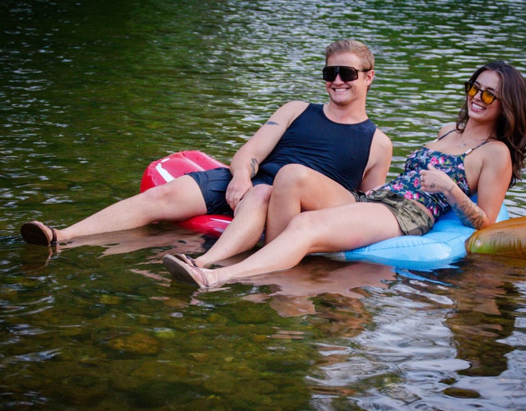 Two people sitting on an inner tube in the lake, wearing protective sunglasses