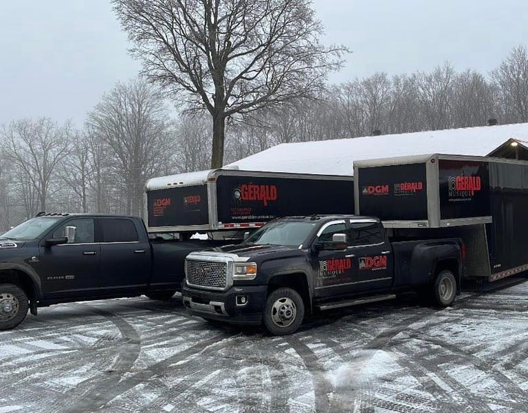 Black Ram and GMC pickup trucks hauling Gerald Musique gear trailers in a snowy parking lot.