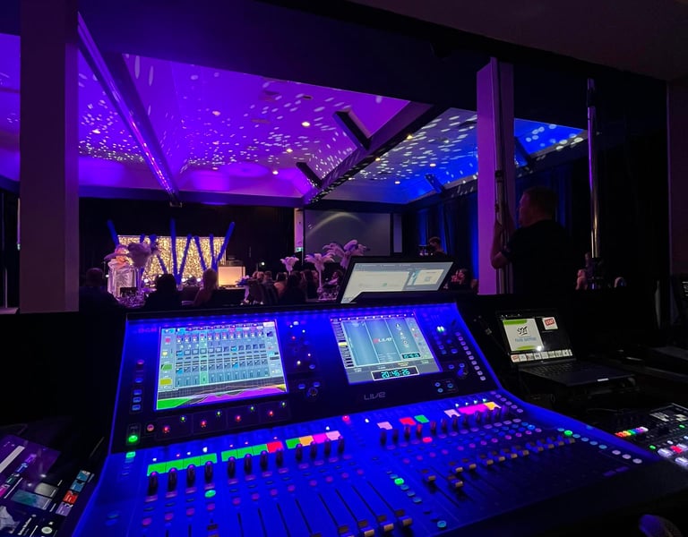 Professional digital audio mixing console with glowing blue lights at a live event venue.