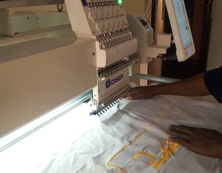 Professional multi-needle embroidery machine stitching yellow thread onto white fabric with a touchscreen control panel.