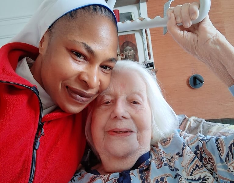 A smiling caregiver and an elderly woman holding a bed trapeze handle during home elder care.