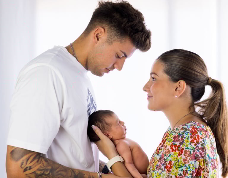 Sessió de fotos newborn a Girona amb una bebè dormint als braços dels pares en estudi fotogràfic