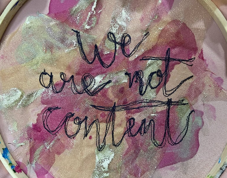 machine embroidered text which says 'we are not content' in cursive writing on a pink background