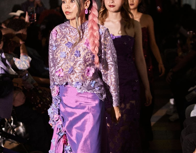 Fashion model wearing a purple lace floral blouse and silk skirt during a runway show.