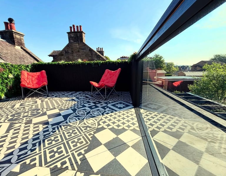 Modern rooftop terrace featuring patterned monochromatic floor tiles and two red folding chairs under a clear blue sky.