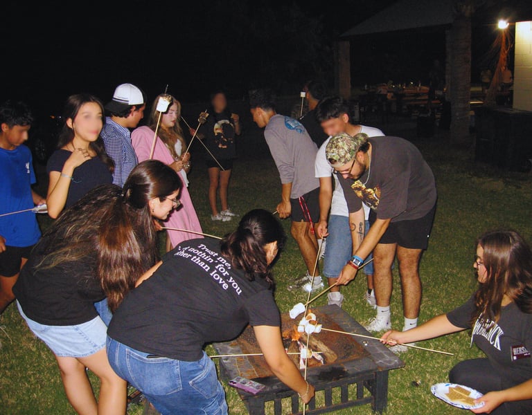 With young people roasting marshmallows outside by a campfire.