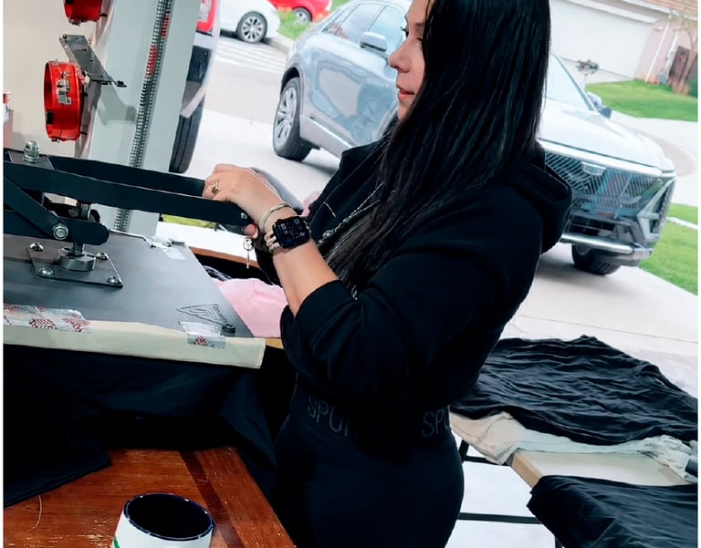 A woman uses a professional heat press machine to print custom designs onto black t-shirts.