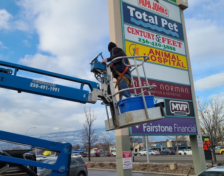 "Technician performing maintenance on a large outdoor sign, ensuring optimal function.