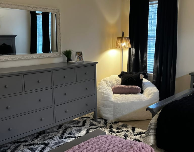 Modern bedroom featuring a gray dresser, white shag bean bag chair, and black curtains.