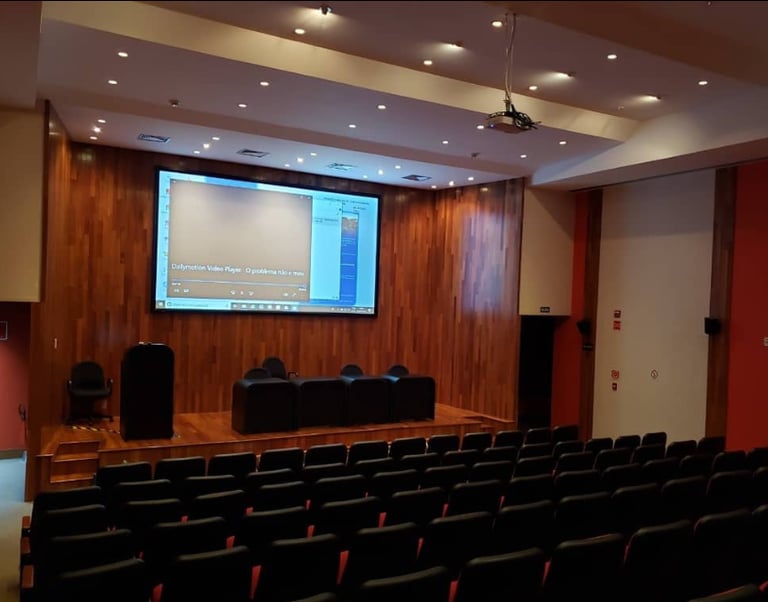 Tela elétrica e projetor em auditório grande com cadeiras pretas