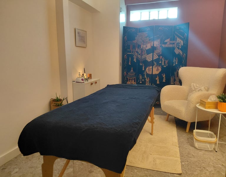 Holistic massage room with a blue therapy table, white armchair, and decorative privacy screen.