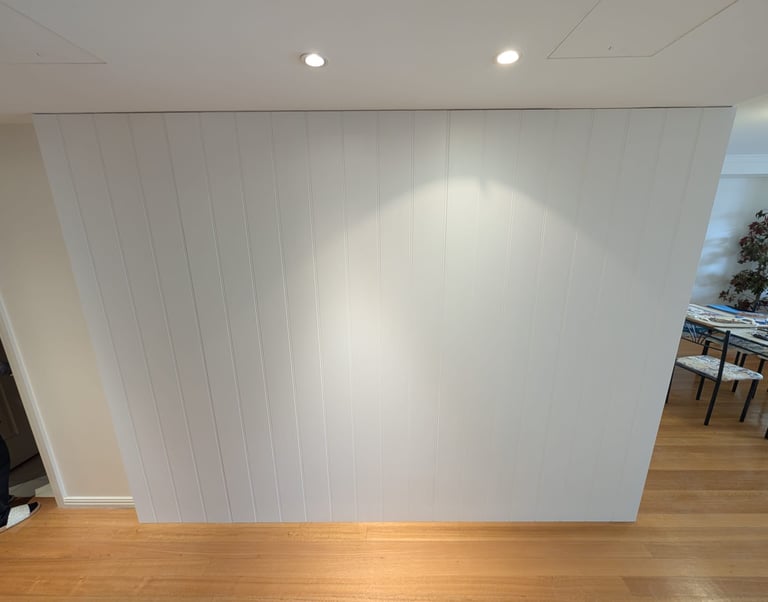 Modern white vertical shiplap accent wall with recessed spotlighting and oak hardwood flooring.