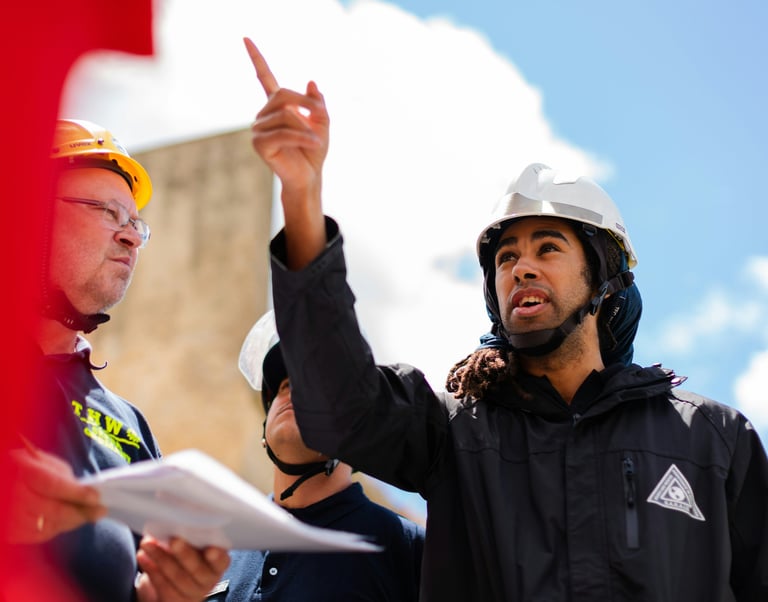 Professional construction site supervisor in a hard hat pointing toward project plans during a team meeting.