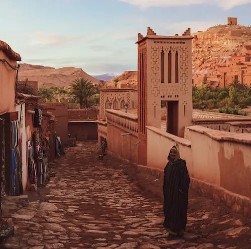 Alleyway in Ait Benhaddou with terracotta walls, man in traditional Moroccan dress in foreground