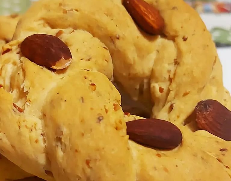 Traditional Italian taralli dolci biscuits topped with whole almonds on a white plate.