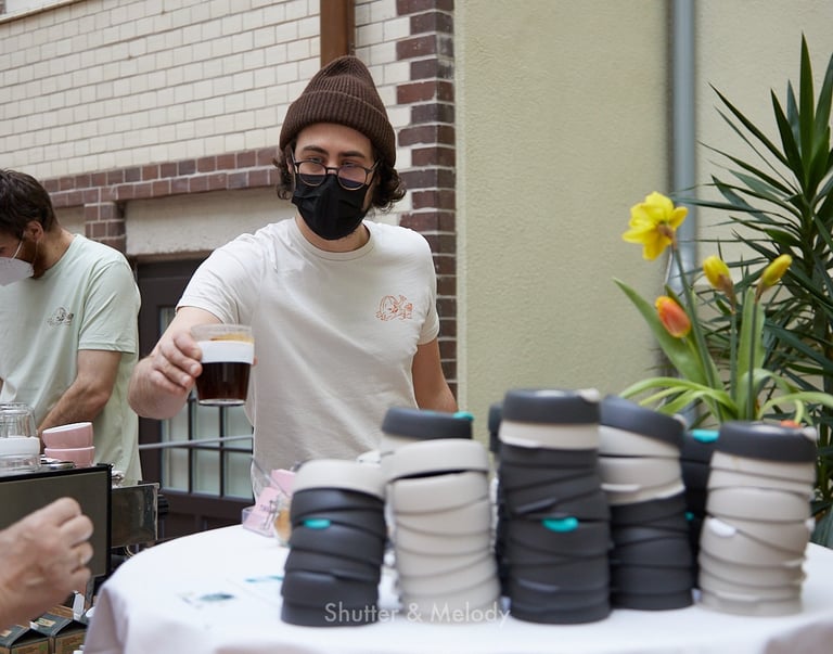 Ein Barista mit einer schwarzen Maske, der einen Kaffee serviert.
