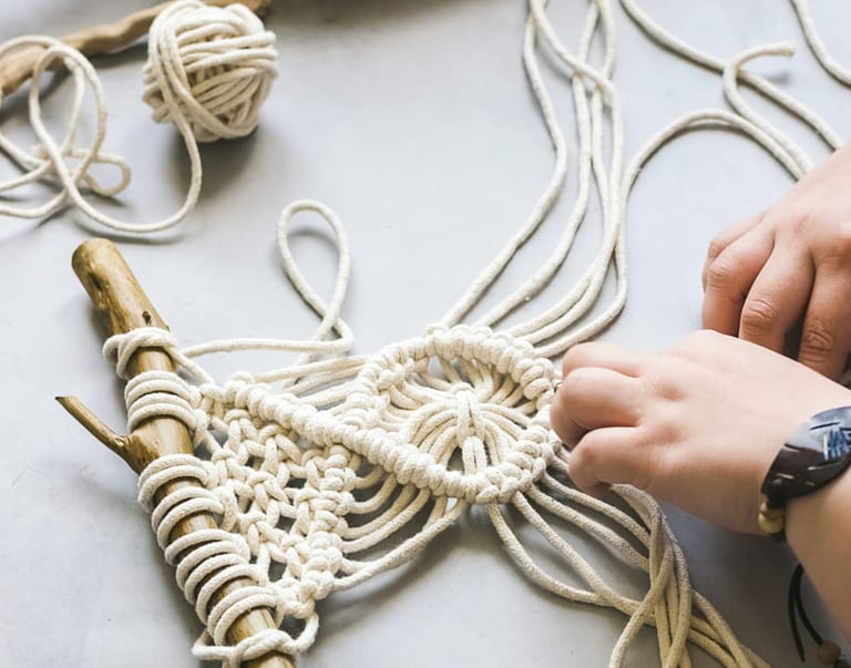Manos elaborando un tapiz de macramé hecho a mano utilizando cordón de algodón blanco