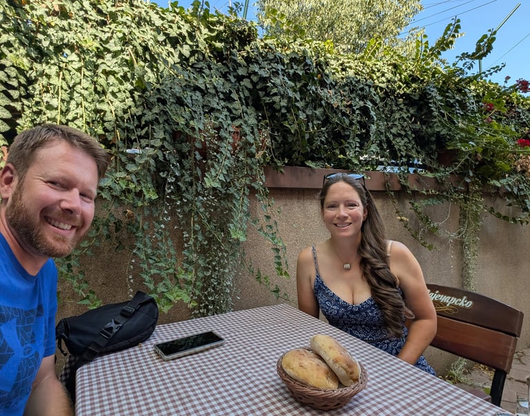 Mooseand Bugs sits at an outdoor restaurant table with fresh bread in front of a lush ivy wall.
