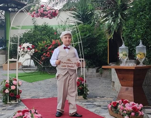 Garoto de nove anos, com um vestimenta classica de cor beje e camisa branca, e usando um boina beje.