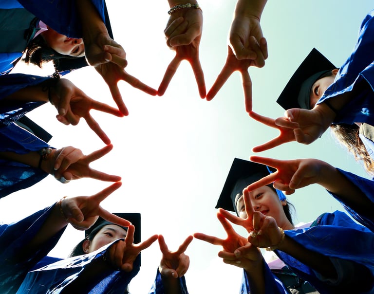 Group of graduates in blue gowns and caps forming a star shape with their fingers while celebrating 