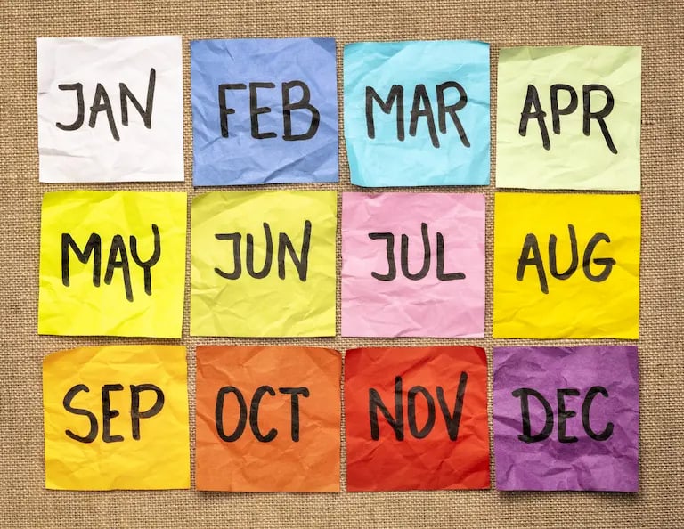 Twelve colorful sticky notes with months of the year arranged on a burlap background for calendar planning.