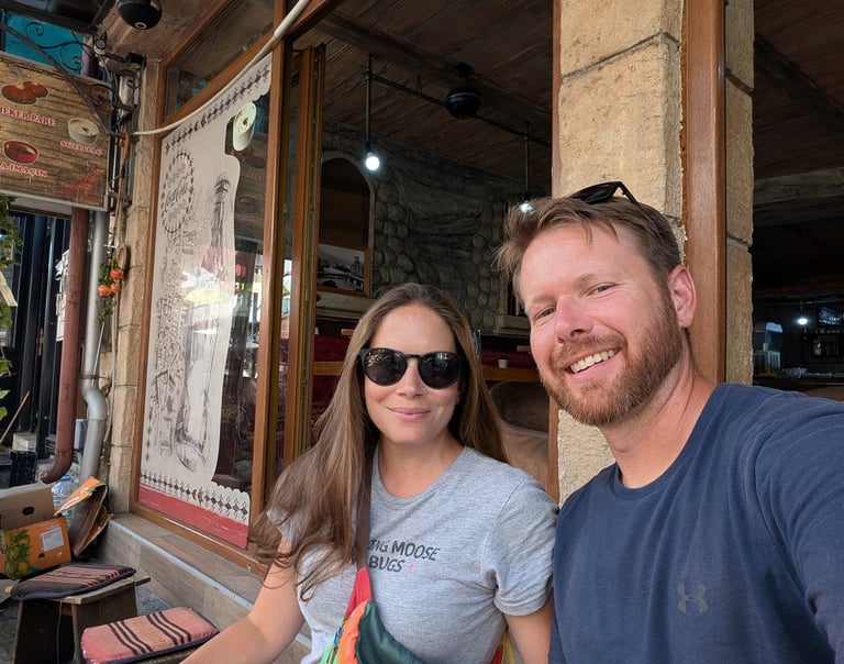Don and Samantha taking a selfie while sitting outside a rustic cafe during their summer travel vacation.