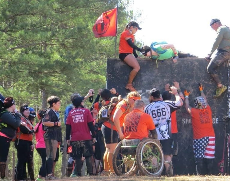 people helping other athletes over a wall at a spartan race
