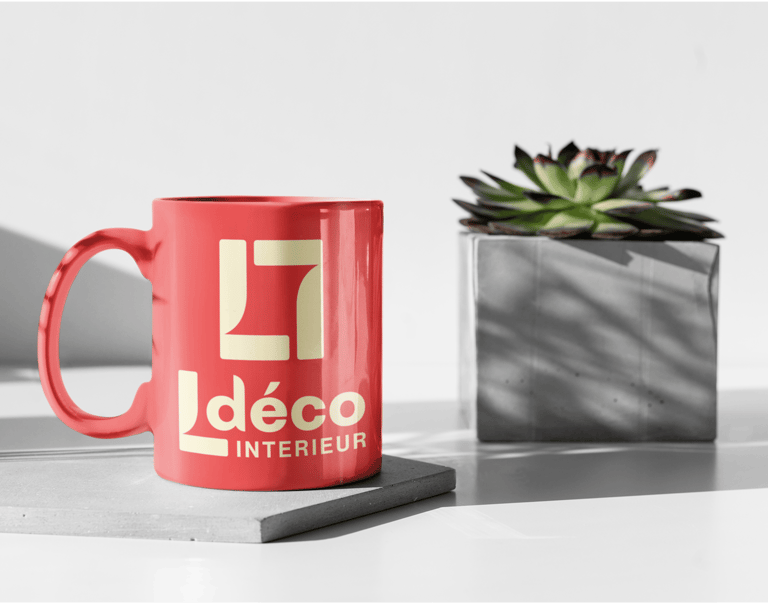 Mug en céramique rouge arborant le logo d'un décorateur d'intérieur à côté d'une plante
