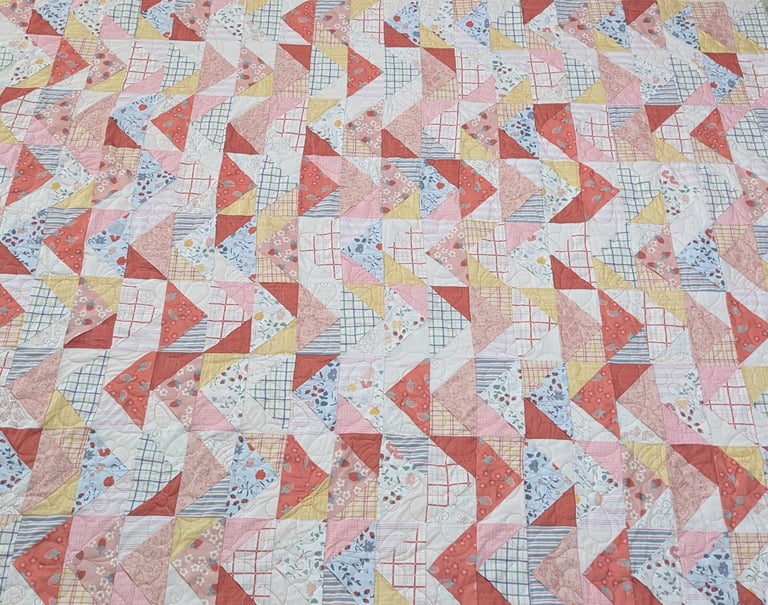 A colorful floral flying geese pattern quilted with a meandering pantograph of daisies