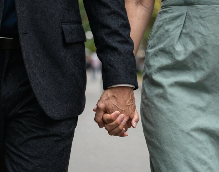 An artistic close-up of a couple's hands intertwined while walking through a North American / US city park. The lighting is soft and professional. The focus is on the intimacy and the elegant textures of their clothing in Dark Charcoal and Sage Green.