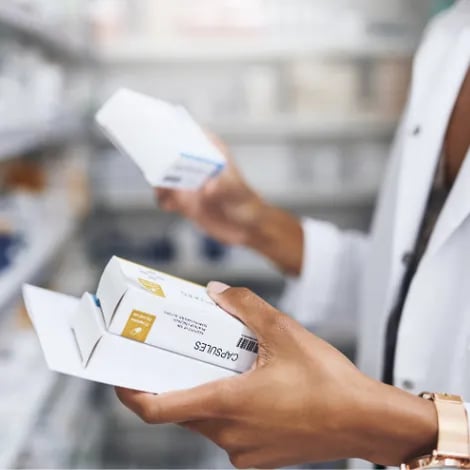 Pharmacist holding medication pill boxes while organizing a pharmacy shelf.