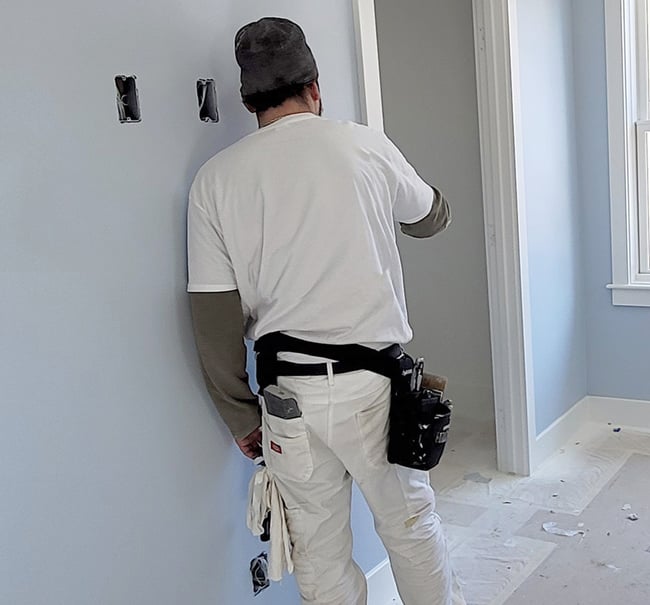 Professional painter in white work clothes inspecting light blue interior walls during a home renovation.