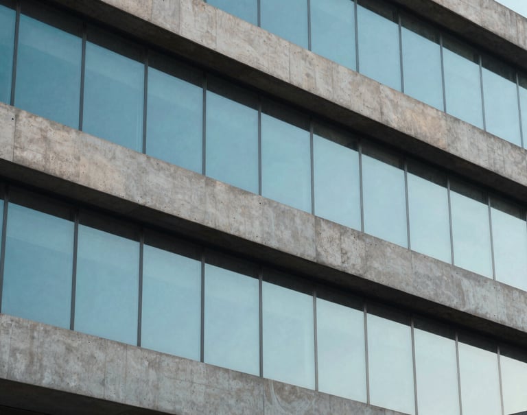 A detailed shot of modern building textures, combining raw concrete in light gray with large panes of glass reflecting a clear baby blue sky, South American urban architecture, minimalist and clean composition.