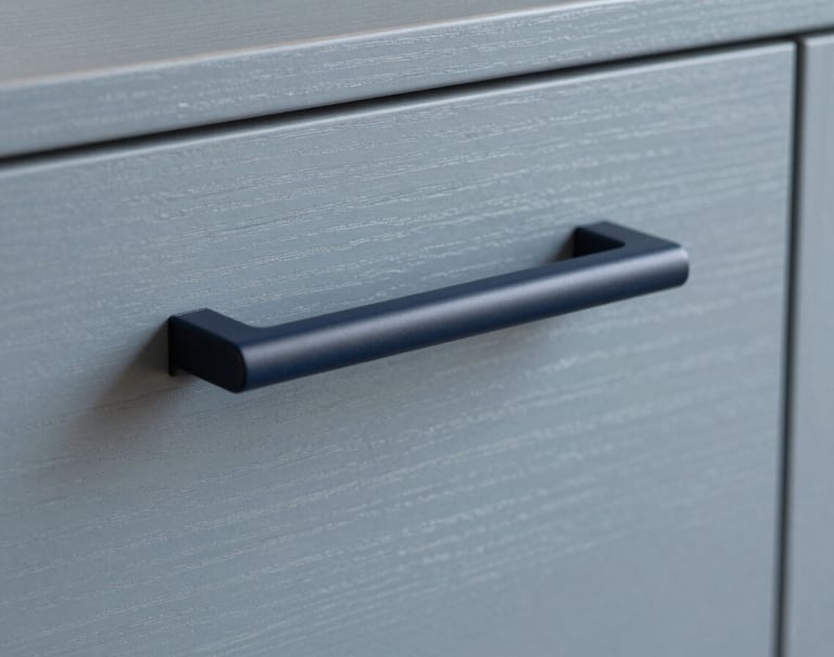 Close-up of a minimalist custom cabinet handle, sophisticated Dark Navy matte finish against a Soft Gray Blue wood surface. Elegant and precise, minimalist Northern European furniture design.