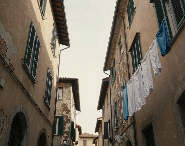A low-angle shot of a narrow Italian street with laundry hanging between buildings. The sky is a soft #F5F0E1 cream. The architecture shows layers of history with peeling #C4B29A paint and deep #262626 shadows, capturing the 'feel in the moment' vibe.