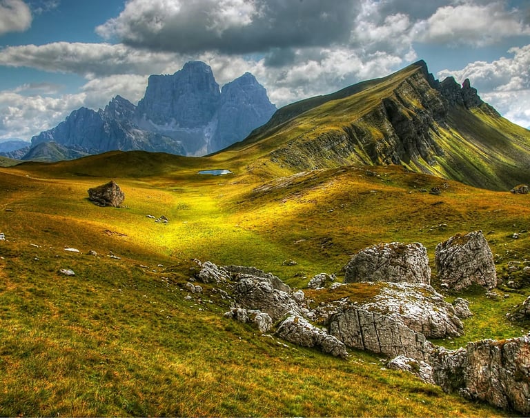 Panoramic view of the green slopes and jagged peaks in the Italian Dolomites under a cloudy sky.